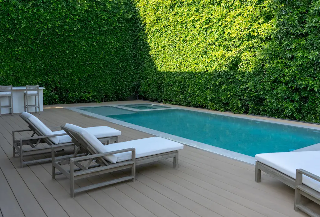 A small backyard deck in West Hollywood. Enclosed by bushes, there is a small pool and a few sun loungers. Depicts decks for small spaces.